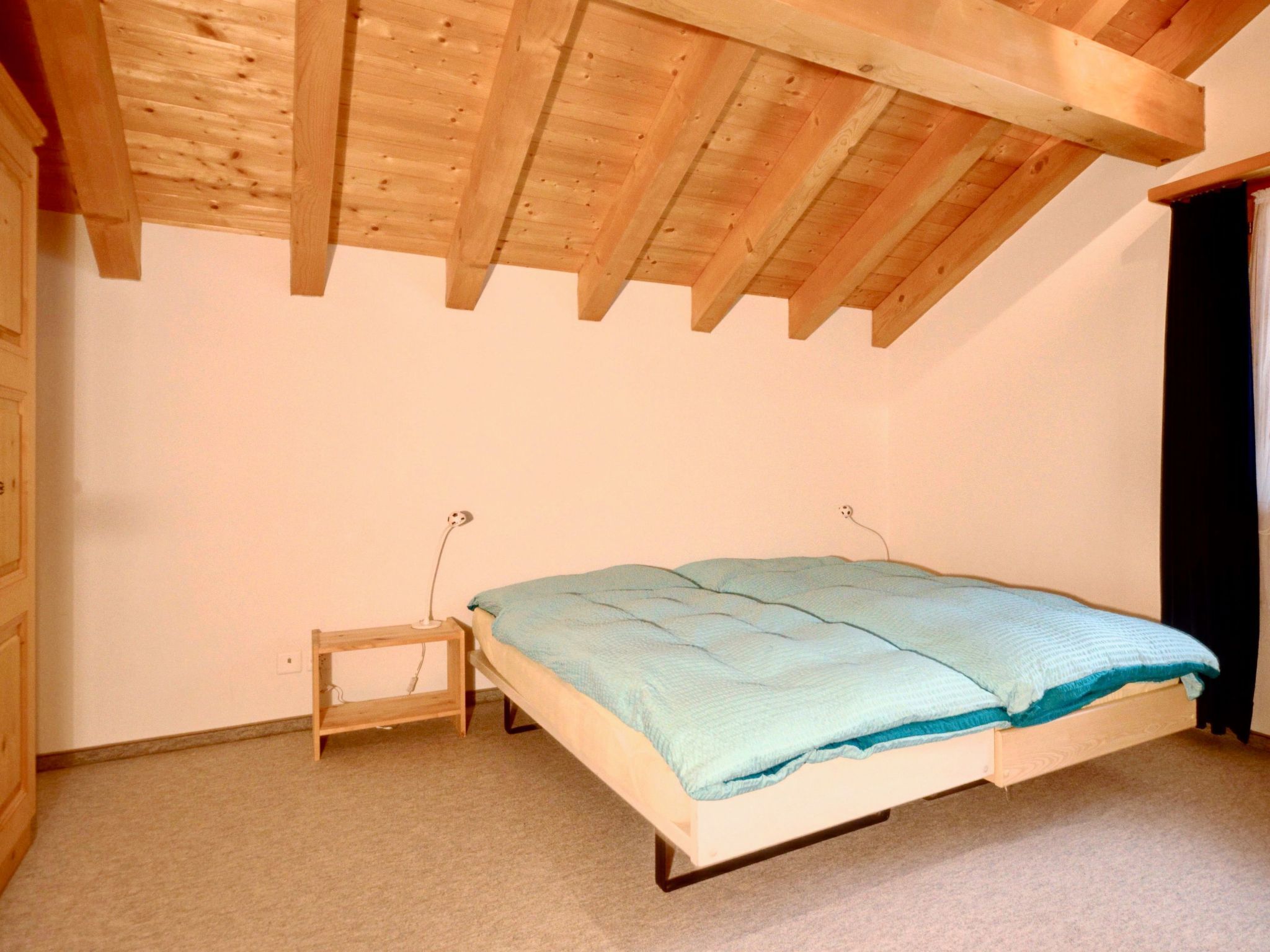 Ein Schlafzimmer mit einem Einzelbett, einem kleinen Nachttisch und einer Holzbalkendecke.