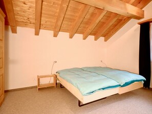 Un dormitorio con una cama individual, una mesita de noche pequeña y un techo de estructura de madera.