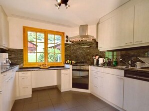 Cocina con armarios blancos, horno empotrado, lavavajillas y ventana con vistas al exterior.