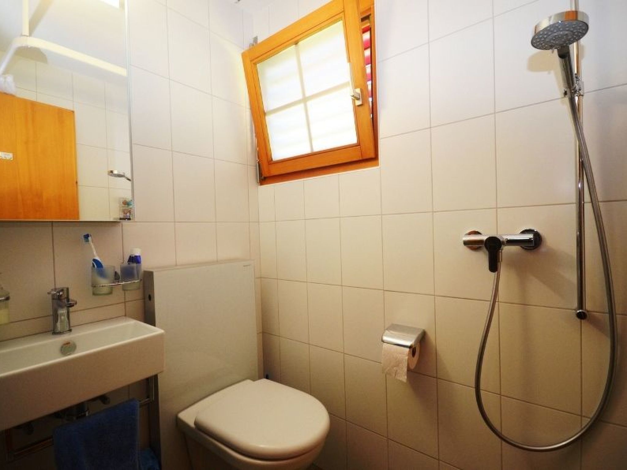 Une salle de bain comprenant des toilettes, un lavabo, un miroir, un porte-serviettes, une douche et une fenêtre.