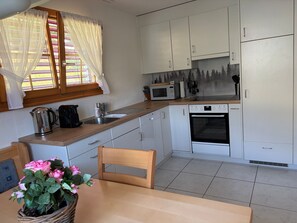 Eine Küche mit weißen Schränken, einer Mikrowelle, einem Backofen, einem Spülbecken und einem Fenster mit Vorhängen.