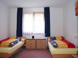 Habitación doble con dos camas individuales, un escritorio, dos sillas, una mesita y una ventana con cortinas.