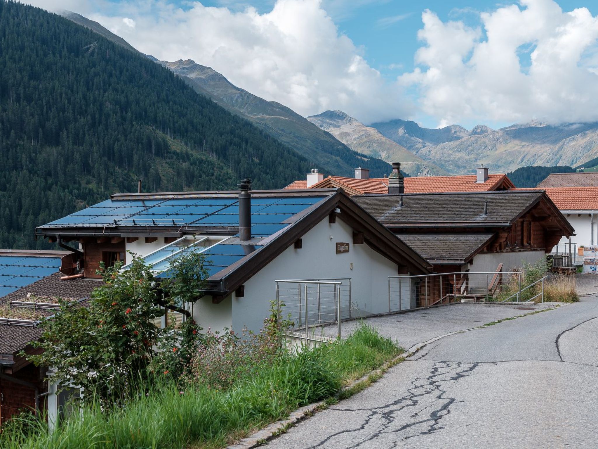 A residential area with solar panels on rooftops, a paved road, and mountainous terrain in the background.