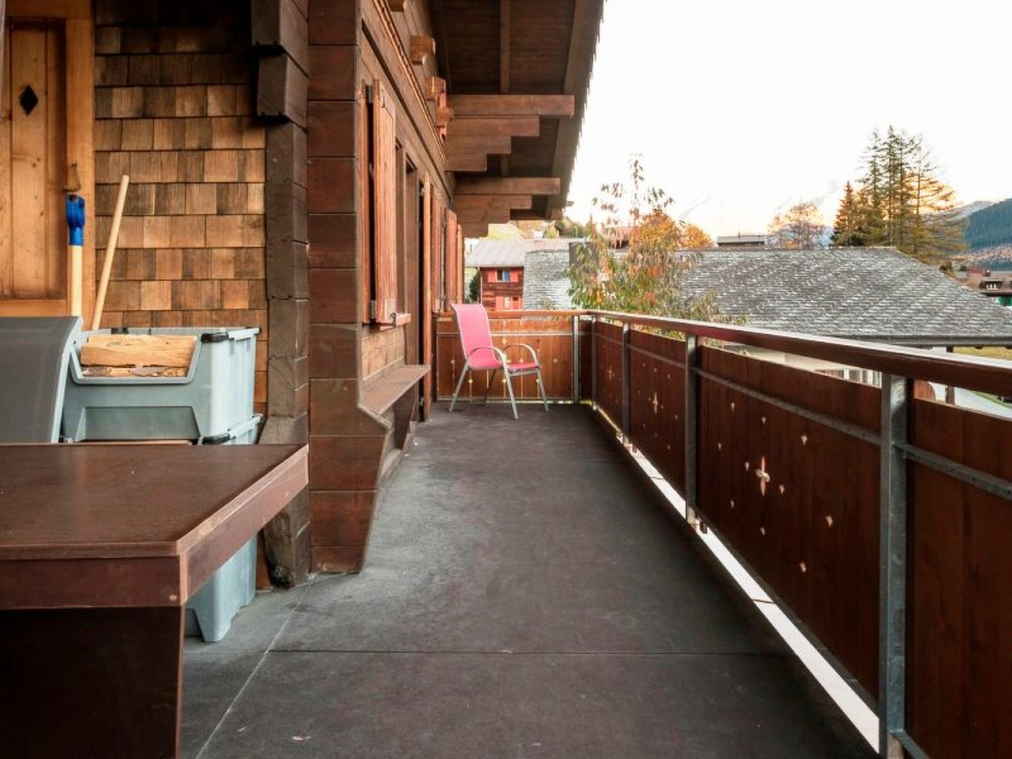 Een balkon met houten leuning, een stoel en een tafel met een prullenbak.