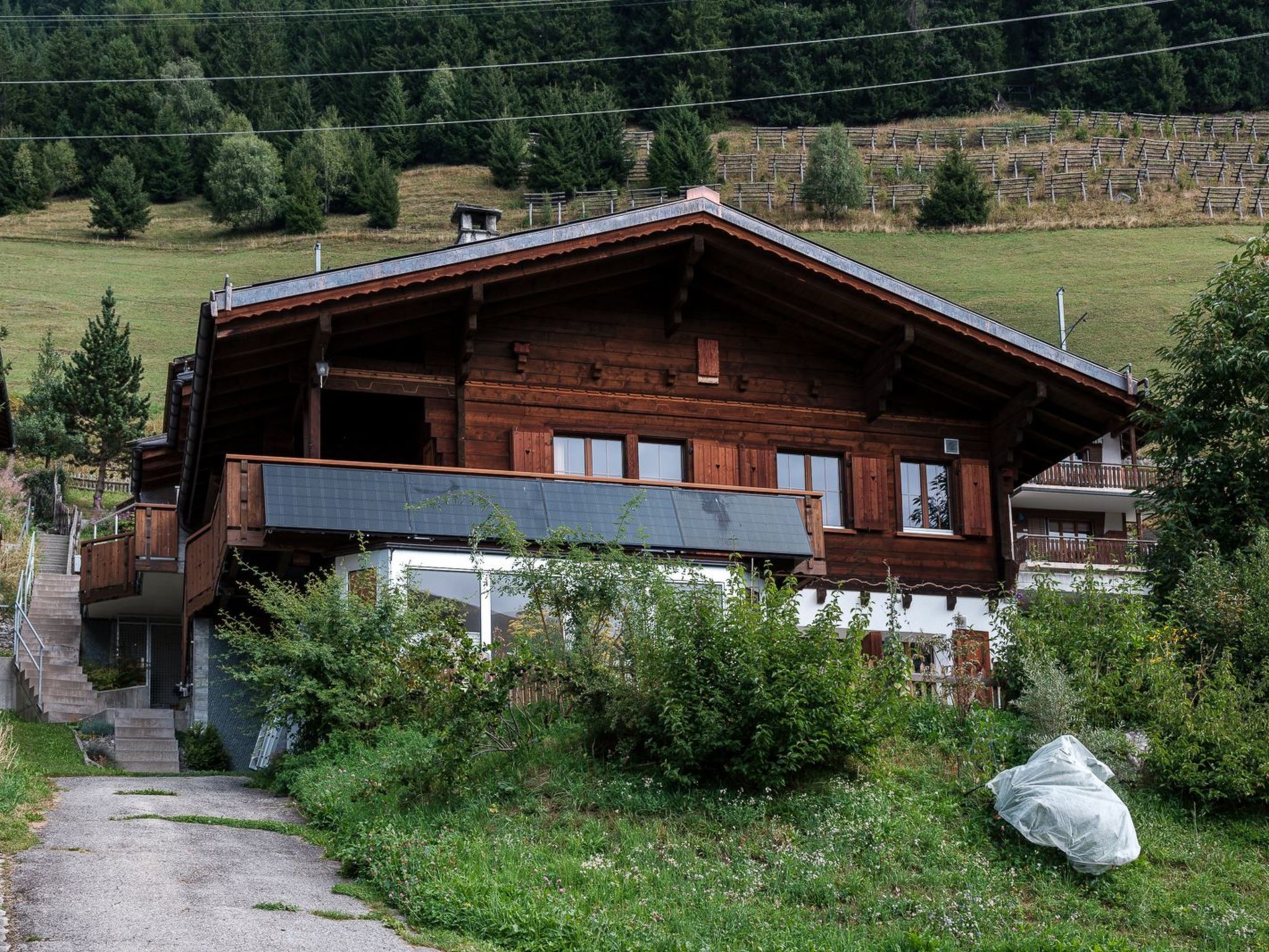 Eine Holzchalet mit Balkon, umgeben von viel Grün und einer Steinmauer im Hintergrund.