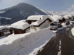Een met sneeuw bedekte bergweg met houten gebouwen, een geparkeerde auto en een sneeuwduin.