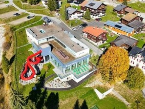 Vue aérienne d’un quartier résidentiel avec des maisons, une aire de jeux et un grand toboggan rouge.