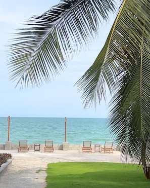 A beach view with palm trees, a stone pathway, and wooden chairs.