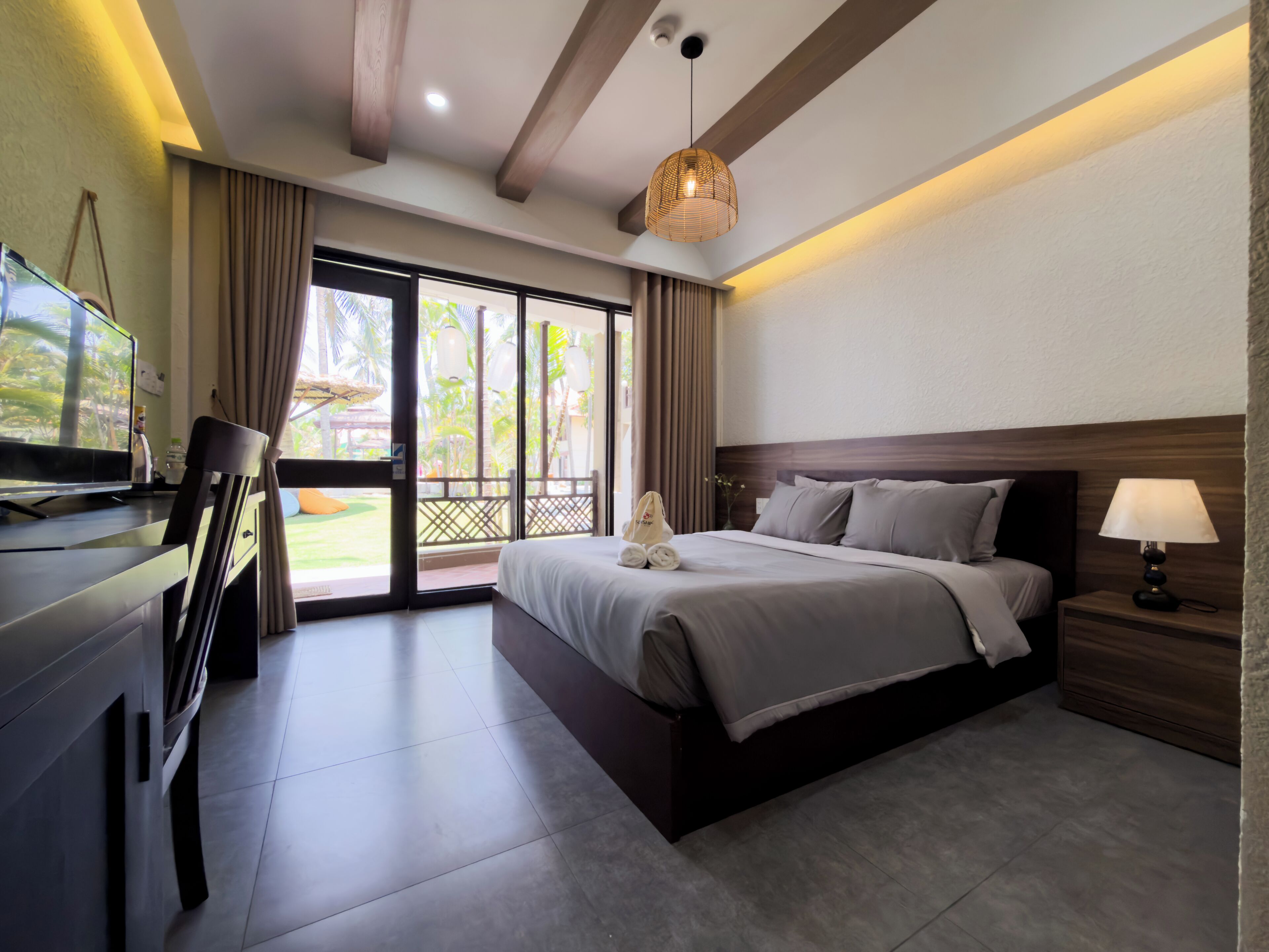 Quarto de hotel com cama, escrivaninha, televisão e varanda com cortinas.