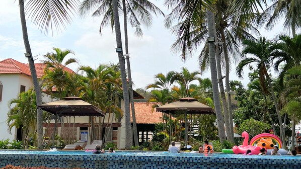 A pool area with lounge chairs, umbrellas, and palm trees.