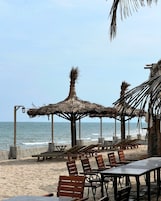 Zona de playa con sombrillas de paja, sillones de madera y vista al océano.