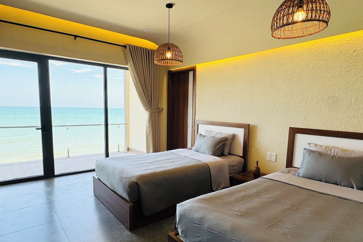 A hotel room with two beds, a large sliding glass door to a balcony, and a view of the ocean.