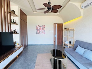 A modern living room with a flat-screen TV, a ceiling fan, a sofa, and a coffee table. - SUNSHINE BEACH RESORT (Phan Thiet)