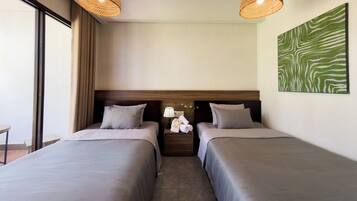 A hotel room with two beds, a nightstand with a lamp, a wall art piece, and a window with curtains.