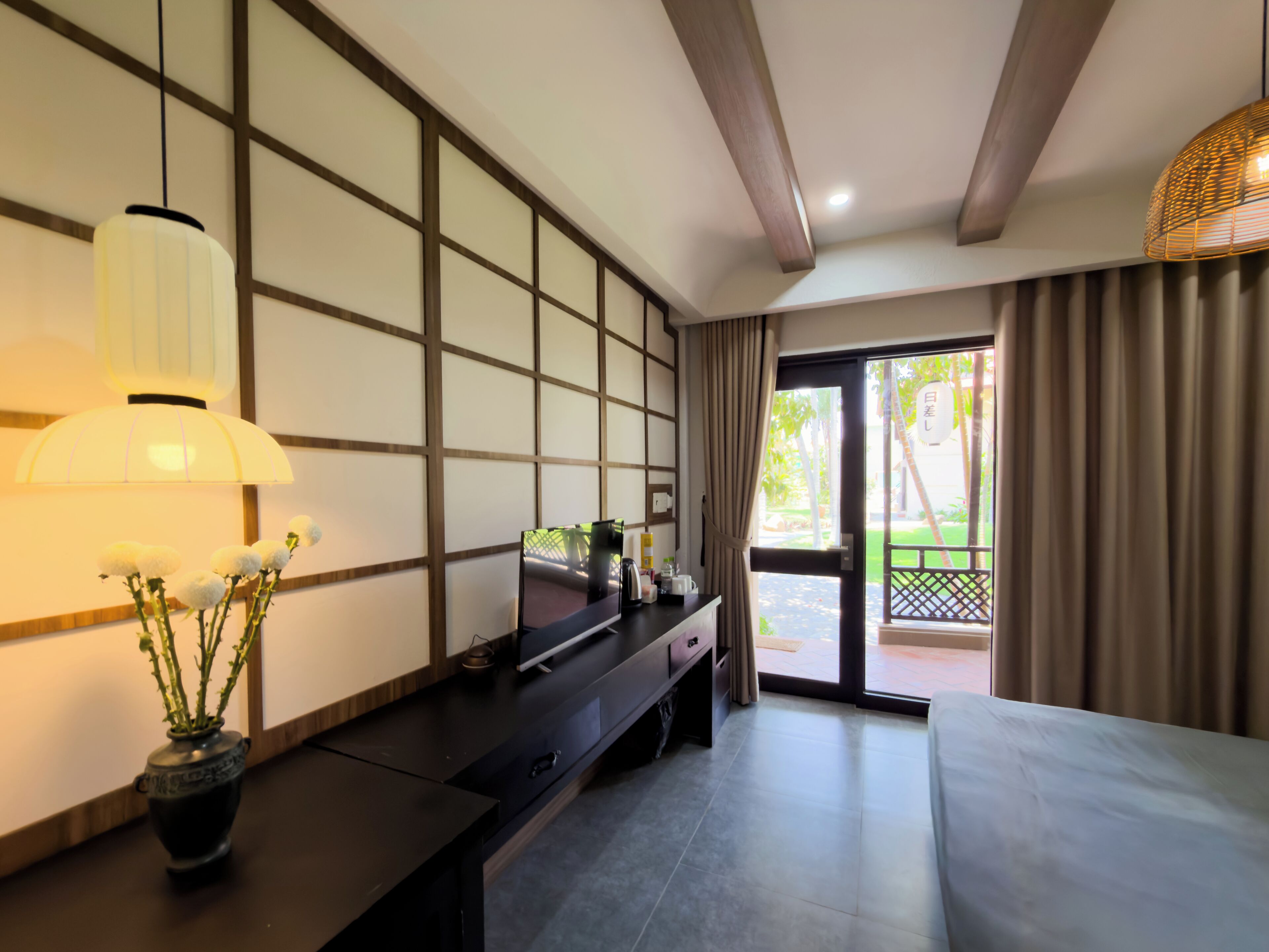 A hotel room with a traditional Japanese-style sliding door, a flat-screen TV on a dark wooden console, a potted plant, and a hanging lamp.