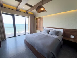 A bedroom with a large bed, a view of the ocean, and a ceiling with exposed beams.
