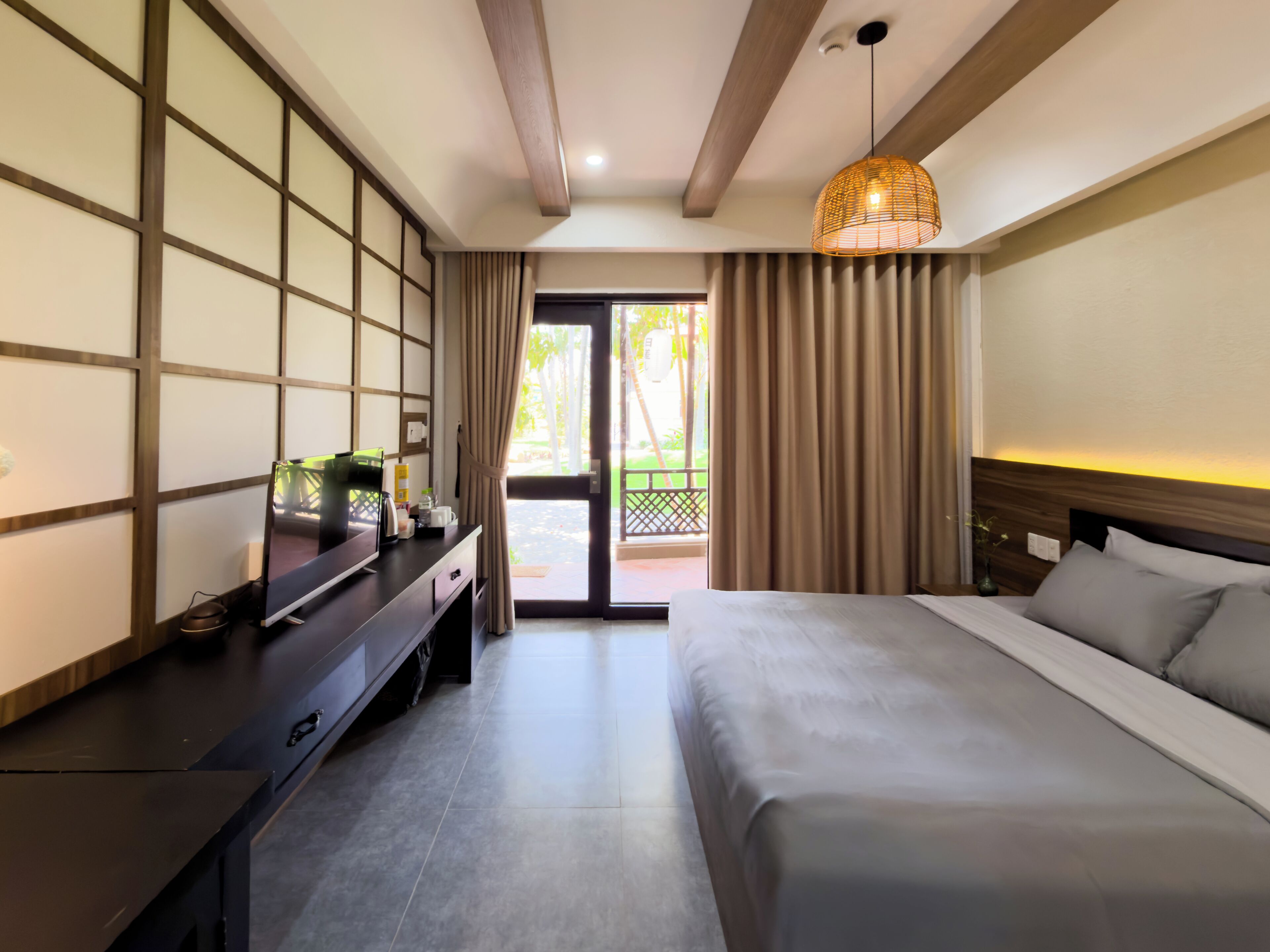 Ein Hotelzimmer mit Bett, Schreibtisch mit Computer, Lampe und Blick ins Freie.