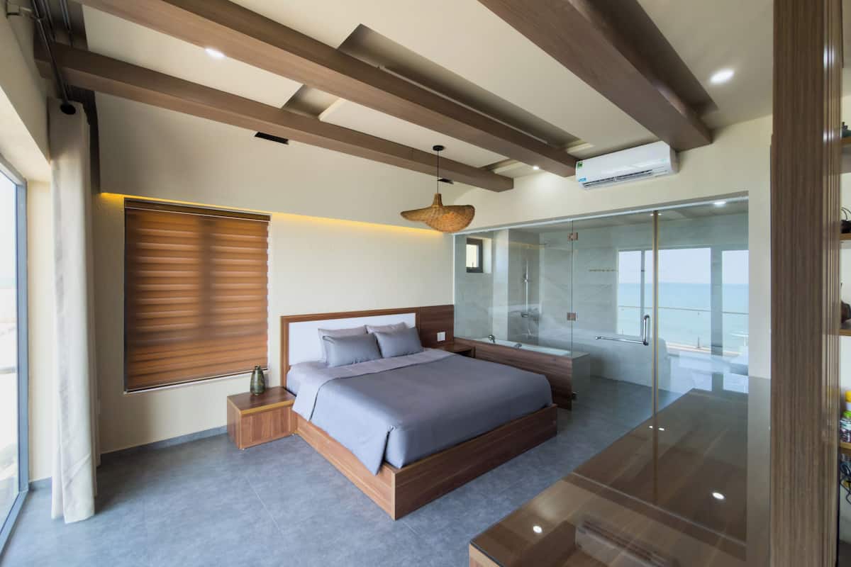A modern bedroom with a large bed, a glass shower enclosure, and a view of the sea.