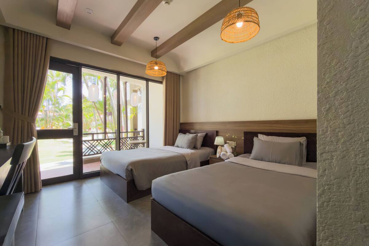 A hotel room with two beds, a balcony, and a view of palm trees.