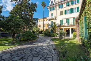 A courtyard with a stone pathway leading to a building with green shutters and a balcony. - Liberty Home In Genova Nervi 2min walk to Sea, Genova, Italy (Genova)