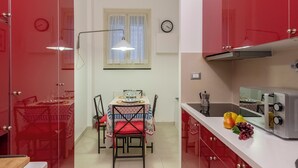 Eine Küche mit roten Schränken, einem Esstisch mit Stühlen, einer Uhr an der Wand und einem Toaster auf der Arbeitsfläche.