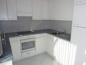 Une cuisine avec des meubles blancs, un évier en acier inoxydable et un four encastré.