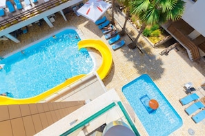 Ein Pool auf dem Dach mit gelber Rutsche, Liegestühlen und einer kleinen Poolanlage.