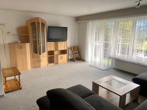 Een woonkamer met een bank, een salontafel, een televisie en een houten kast.
