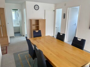 A room with a wooden dining table, four chairs, a clock on the wall, and a wardrobe. - Casa Pignia - Roth, (Laax GR), by Interhome (Laax)
