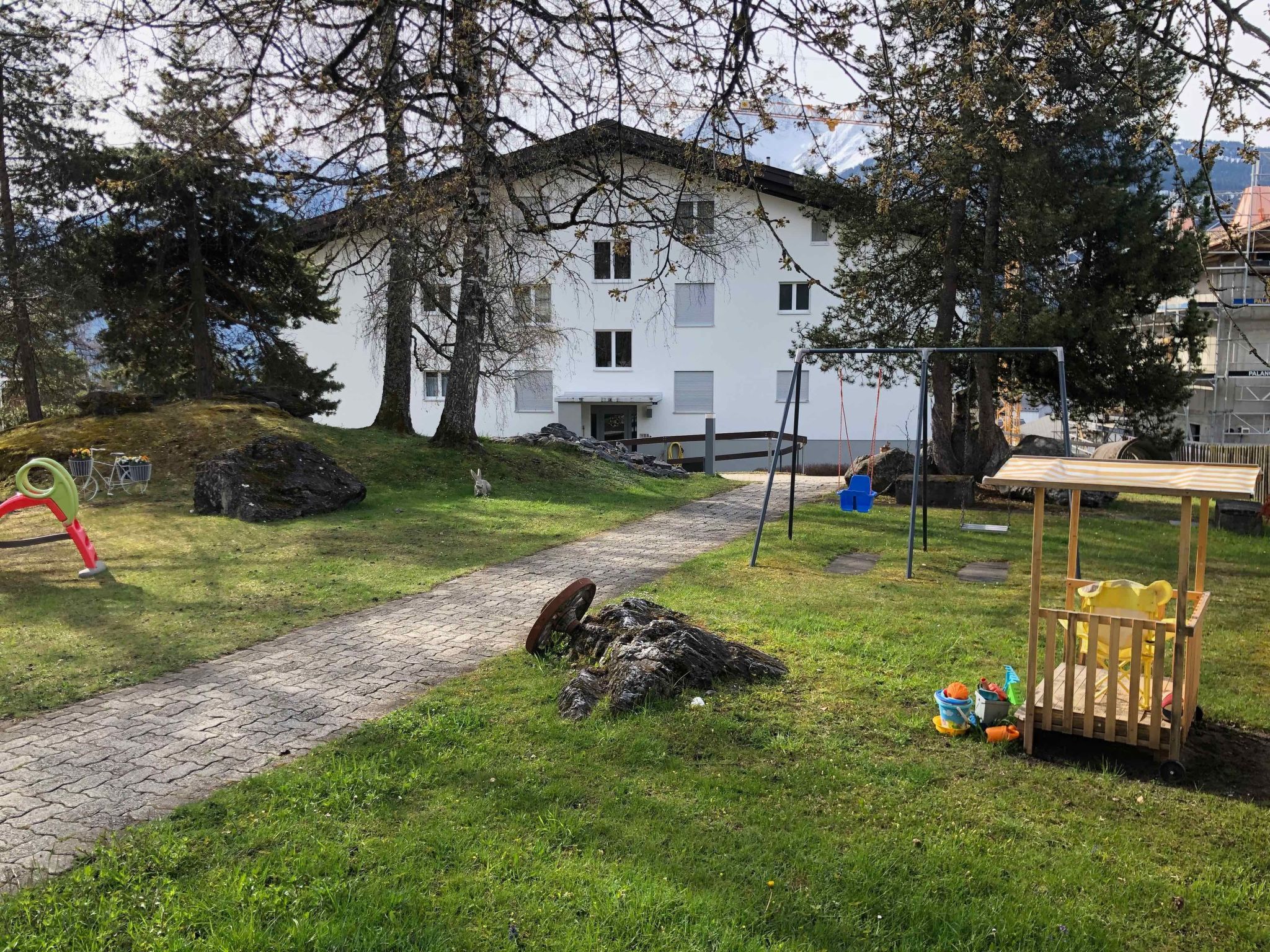 Un chemin mène à un bâtiment blanc où se trouvent une balançoire et un petit espace de jeux.