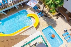 Ein Pool auf dem Dach mit gelber Rutsche, Liegestühlen und einer kleinen Poolanlage.