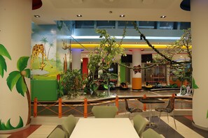 Ein Spielbereich für Kinder mit einer Giraffenmalerei, Zimmerpflanzen und einer Drehscheibe.