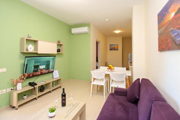 A living room with a television, a sofa, a dining table with chairs, and a kitchen area in the background. - 203 B, One Bedroom Apartment, Vlore, Albania (Vlore)