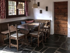 A stone-floored room with a wooden bench seating area, a table, and a door. - Haus 1, (Laax Murschetg), 212 by Interhome (Laax)