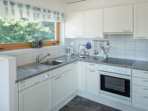 A kitchen with white cabinets, a granite countertop, a coffee maker, and a window with a view of greenery. - Capol-Garten, (Flims Dorf), 2567 by Interhome (Flims)