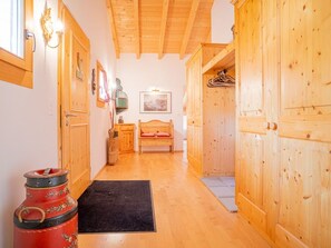 A hallway with wooden walls and ceiling, a bed with red bedding, and a coat rack. - Mira Flem, (Flims Dorf), by Interhome (Flims)