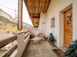 A balcony with a wooden railing, a stone floor, a wooden bench, a small table, and two potted plants. - Mira Flem, (Flims Dorf), by Interhome (Flims)