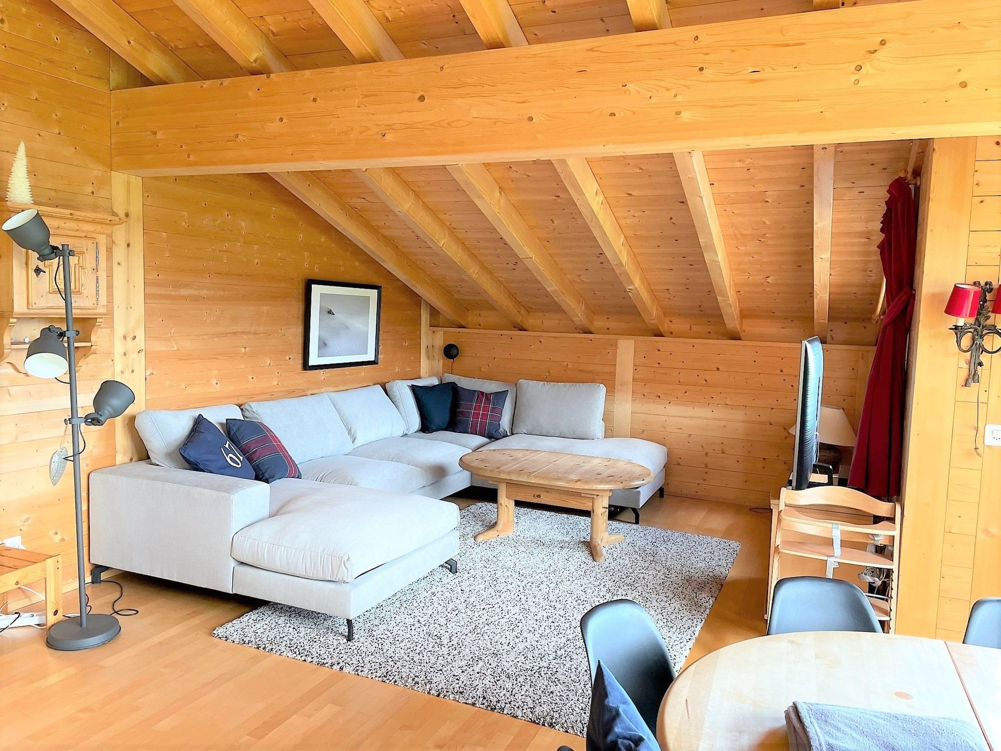 A cozy cabin interior with a sectional sofa, a small wooden table, and a ceiling with exposed wooden beams.