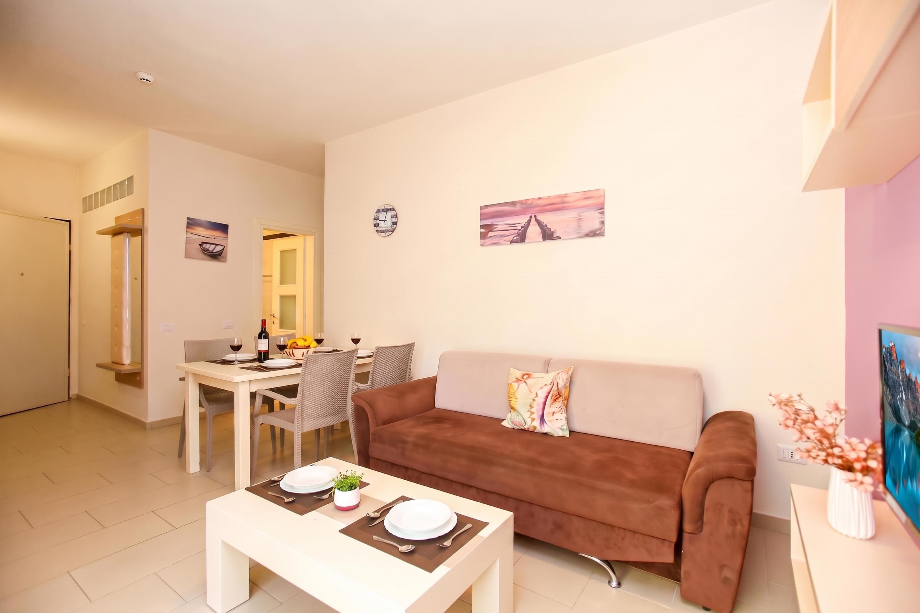A modern living room with a sofa, a dining table set for two, and a small coffee table.