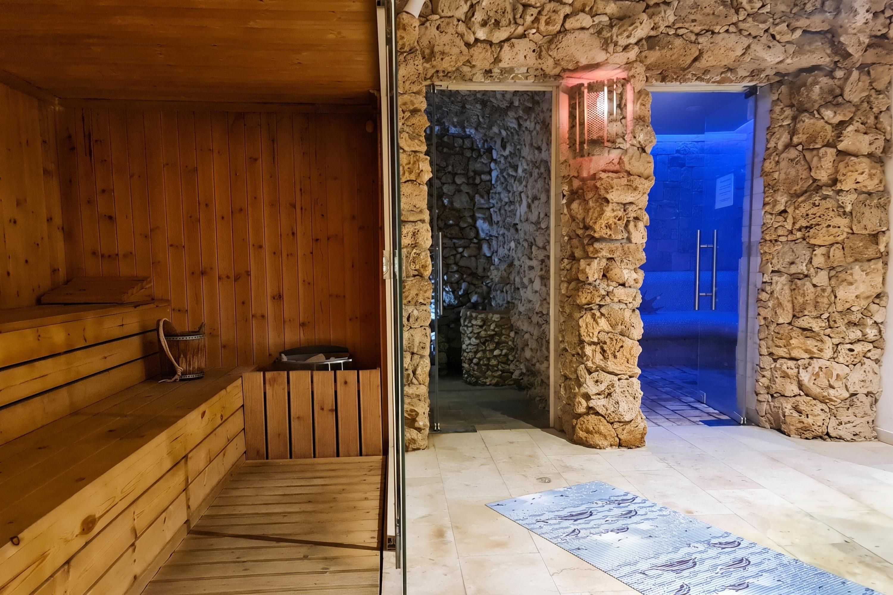 A sauna room with wooden walls and a stone wall leading to a blue-lit area.