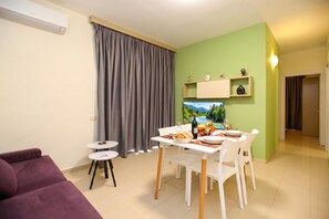 A living room with a purple sofa, a dining table with chairs, a TV, and a green wall. - Apartment in Vlora with Swimming Pool, Vlore, Albania (Vlore)