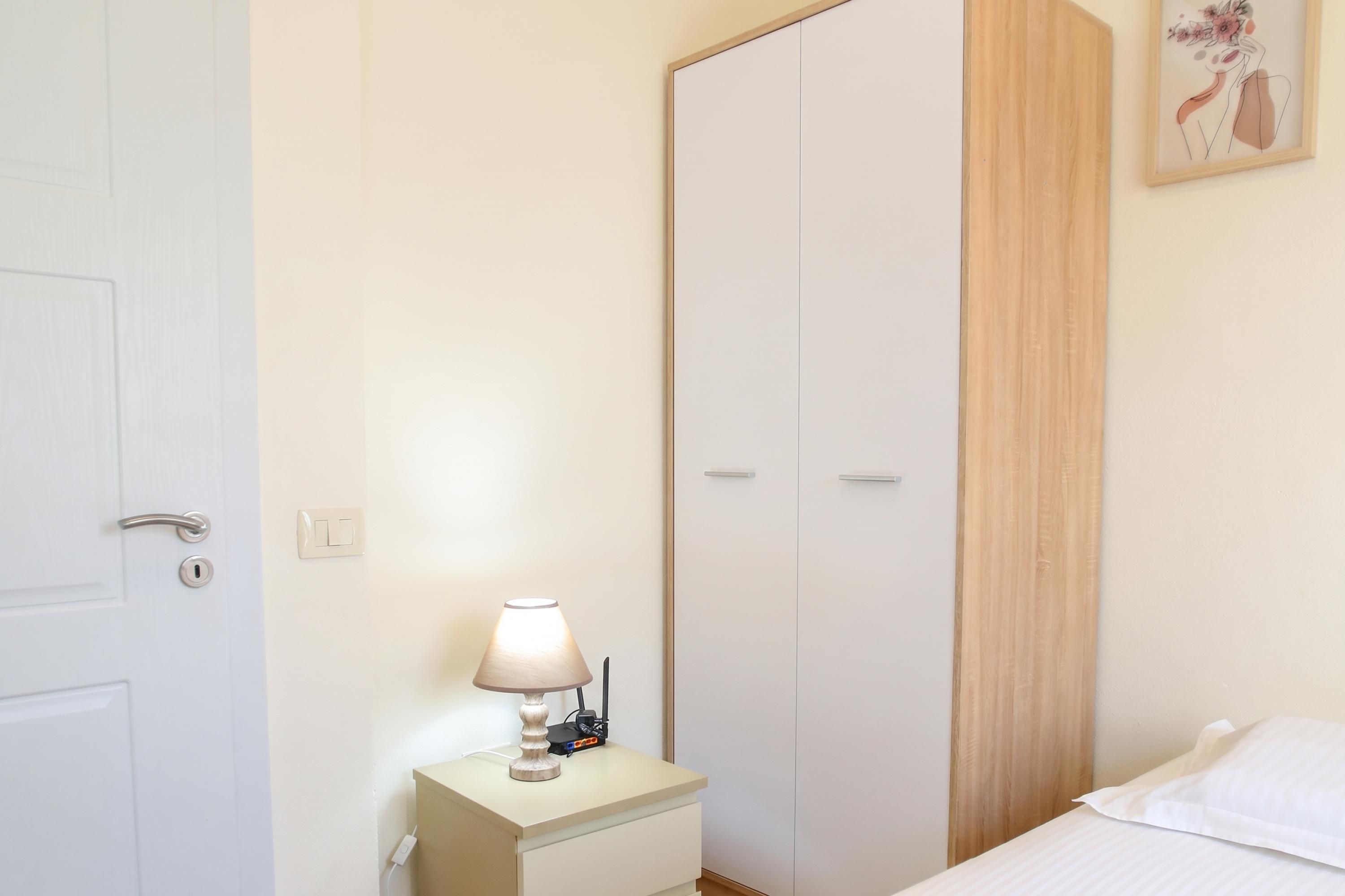 A bedroom with a bed, a bedside table with a lamp, a wardrobe, and a painting on the wall.