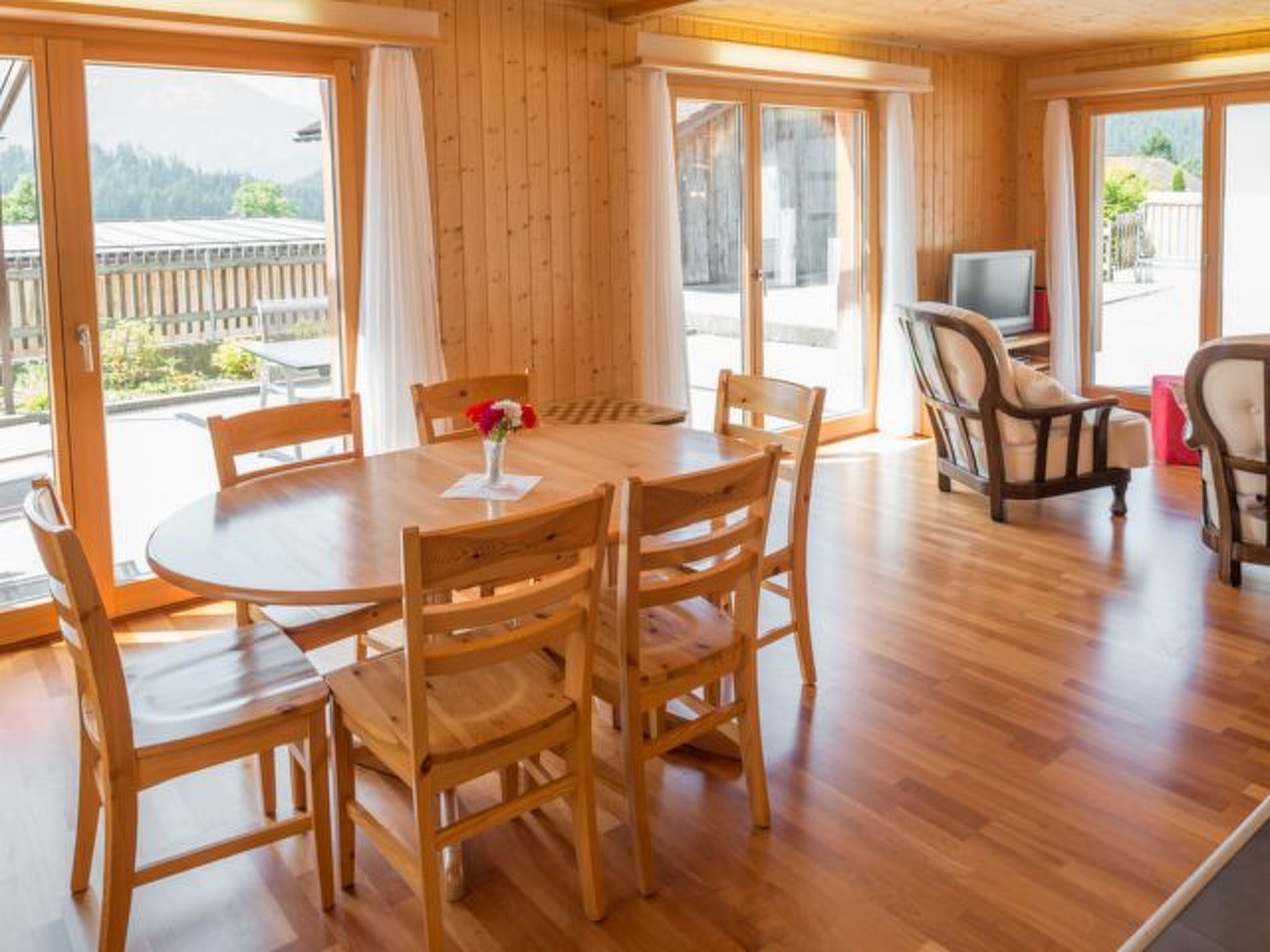 Un intérieur en bois avec une table ronde et des chaises, de grandes fenêtres et un téléviseur.