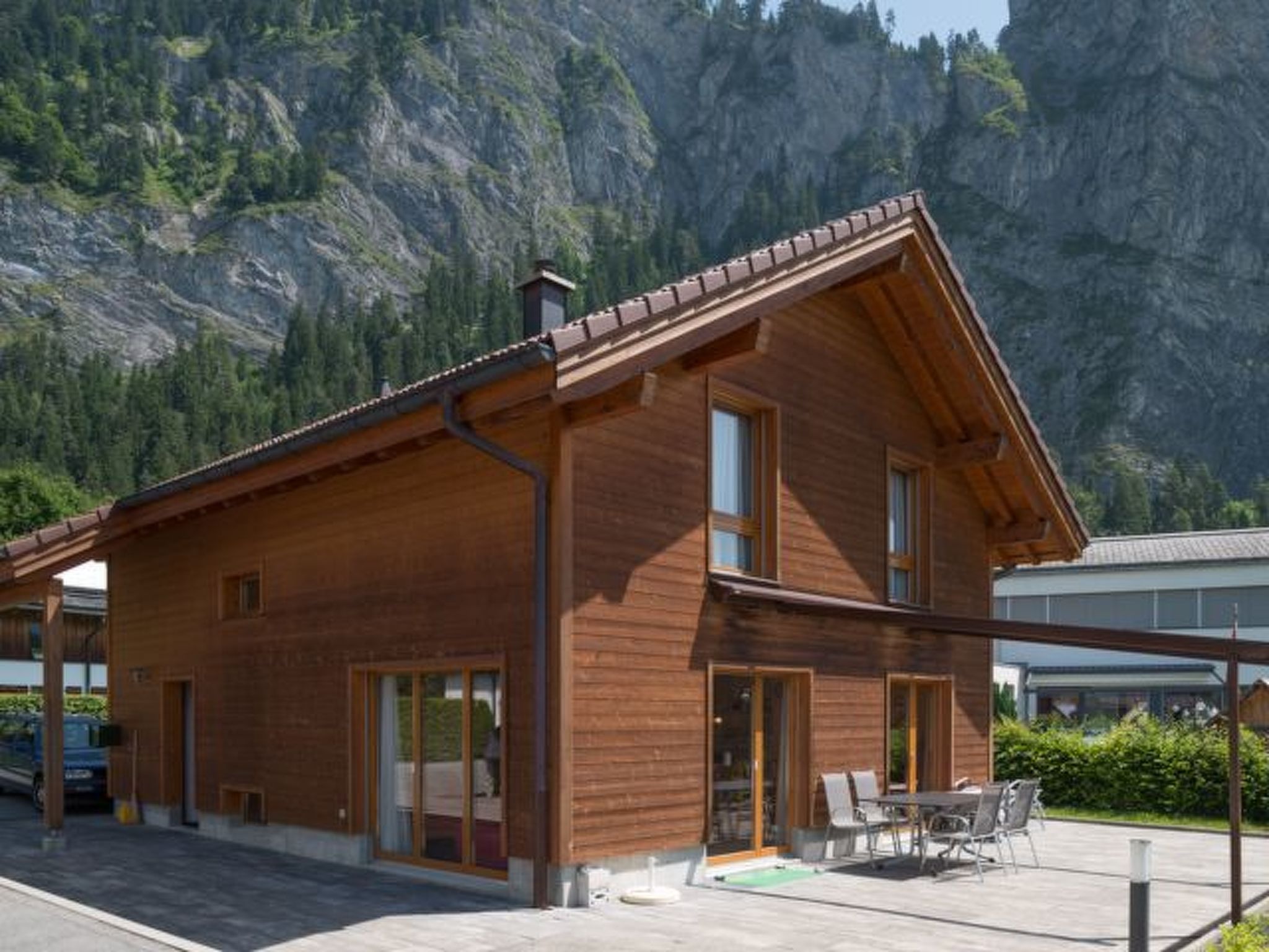 A wooden cabin with a sloped roof, large windows, and a patio area with outdoor furniture.