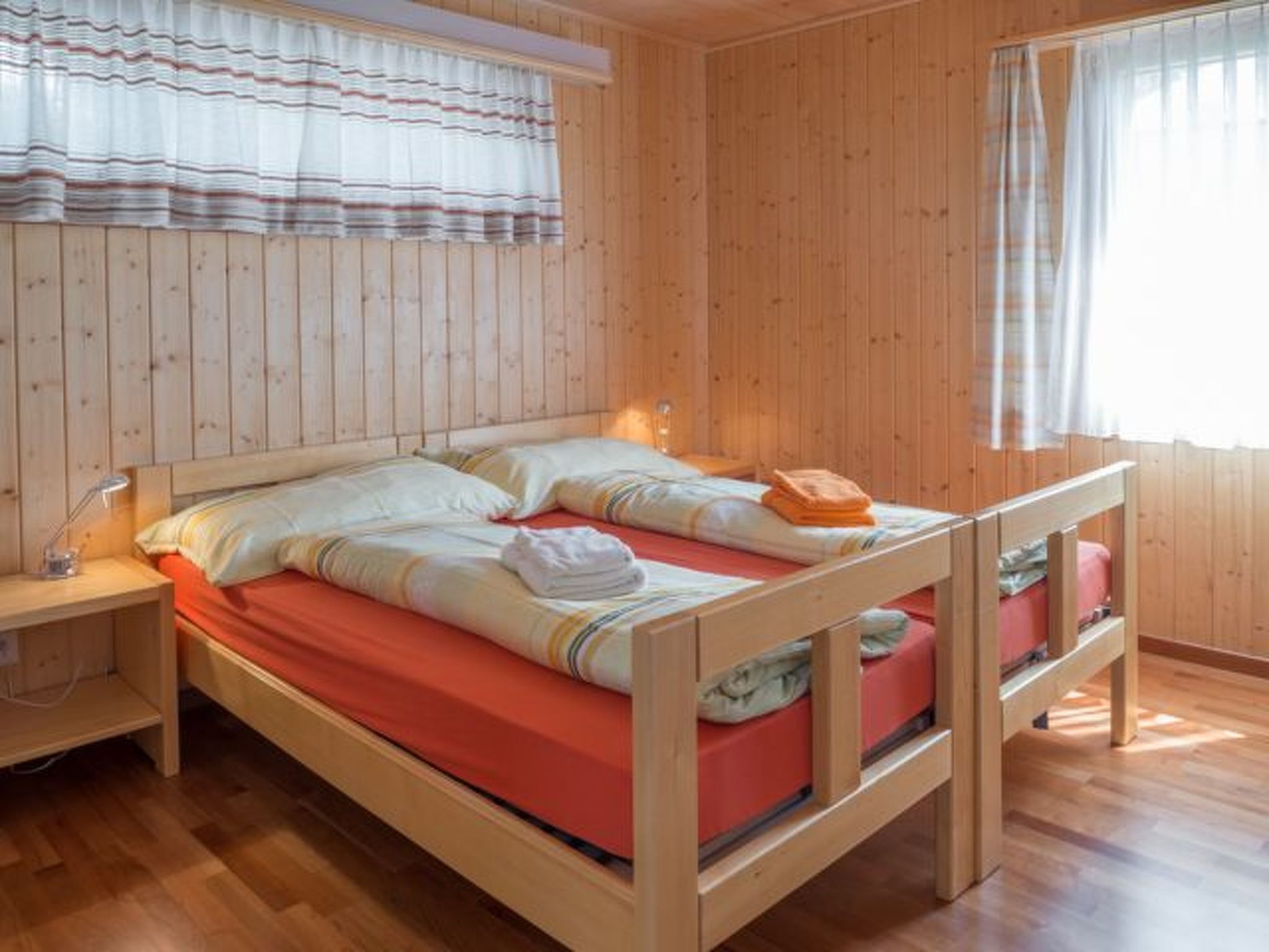 Una habitación de madera con una cama, una mesita de noche y una ventana con cortinas.
