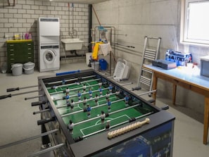 A room with a foosball table, a washing machine, and a table with various items. - Caflisch Jacob und Erika, (Trin Mulin), 500 by Interhome (Trin)