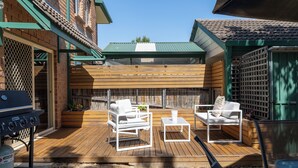 Eine Holzterrasse mit Gartenmöbeln, einem Grill und einem überdachten Bereich mit Gründach.