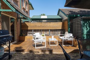 Eine Holzterrasse mit Gartenmöbeln, einem Grill und einem überdachten Bereich mit Gründach.