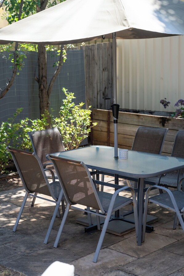 Un patio con una mesa, sillas, una sombrilla y una valla de madera al fondo.