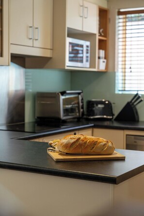 Una cocina con hogaza de pan sobre tabla de cortar, un tostador y un microondas.